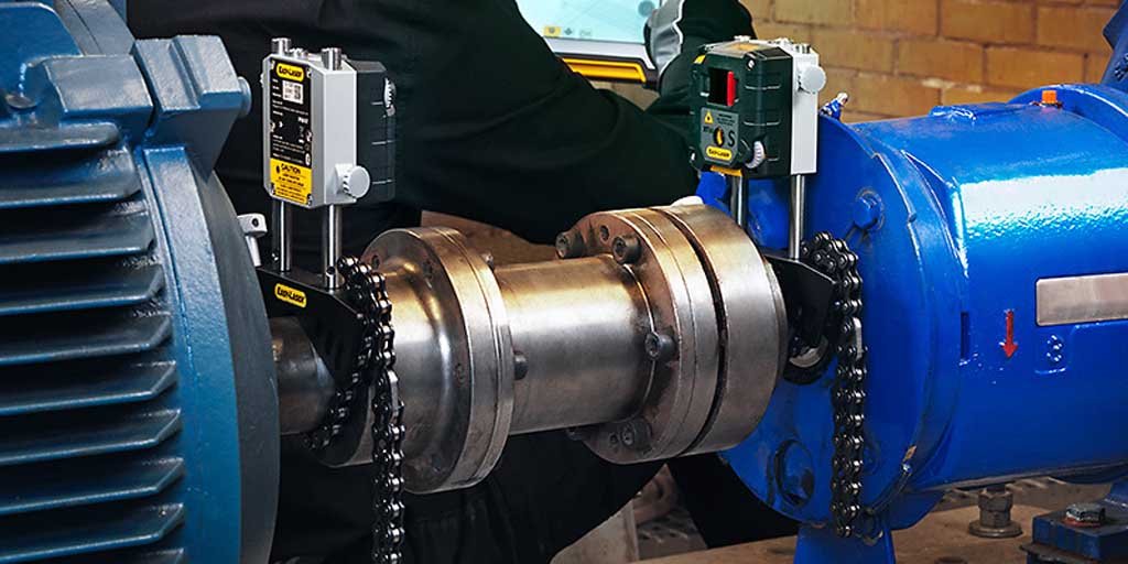 Close-up of industrial shaft coupling connecting a blue motor and blue machine housing with sensors and chain guards attached.