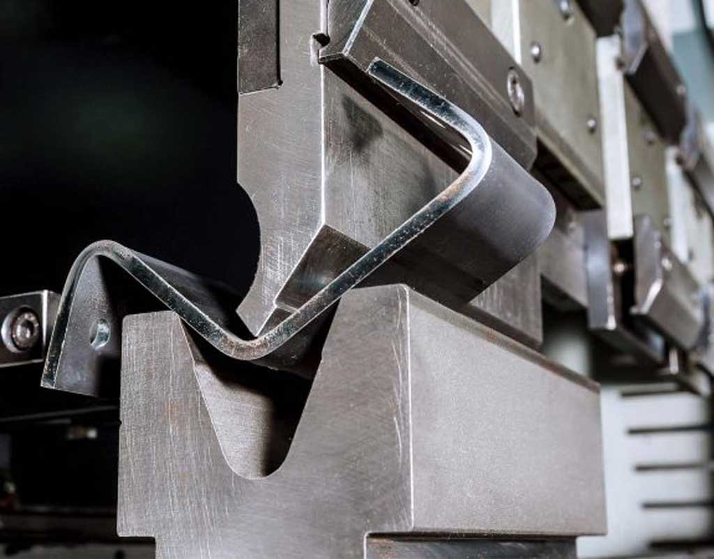 Close-up of a metal press brake machine bending a sheet of metal into a V-shaped angle.