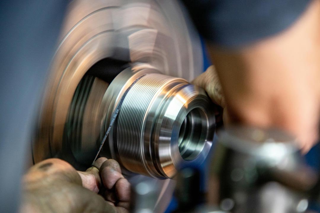 Close-up of a person using a file tool on a rotating metal lathe piece in a workshop.