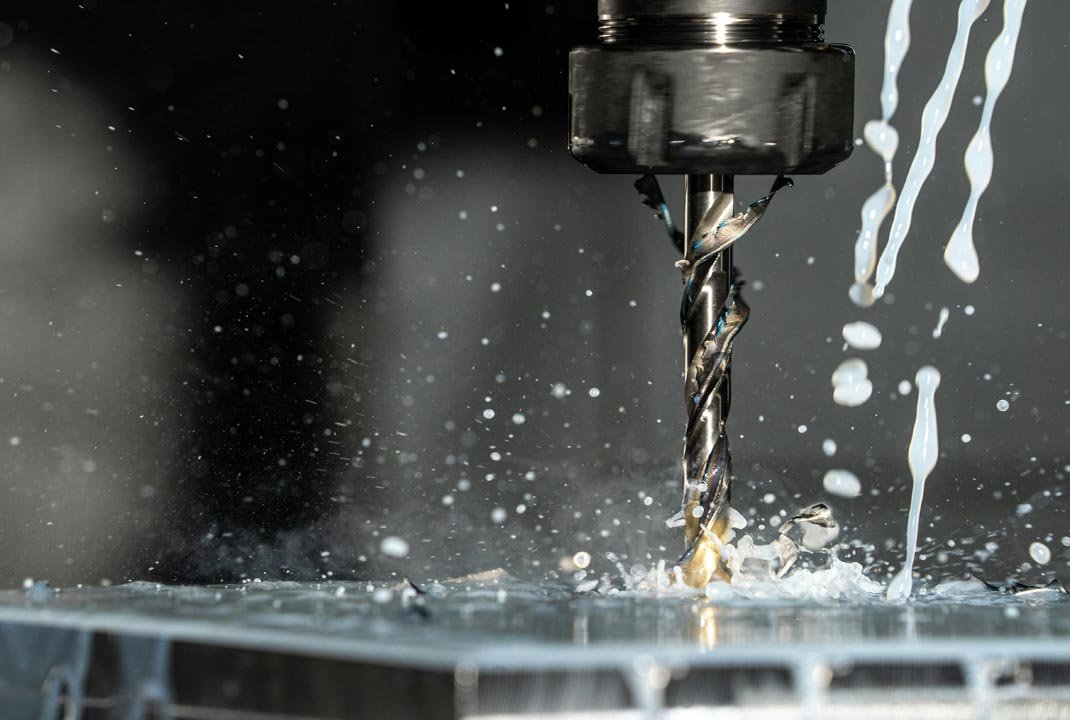 Close-up of a drill bit cutting metal with coolant fluid splashing around.