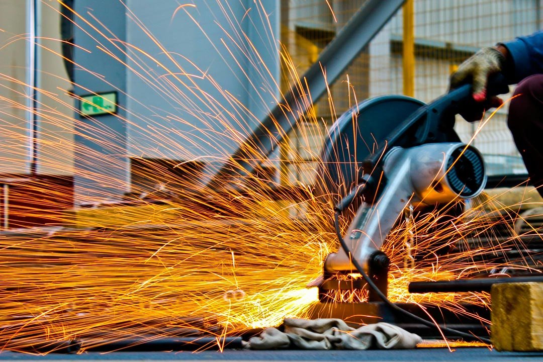 Worker using an angle grinder producing bright orange sparks in an industrial setting.