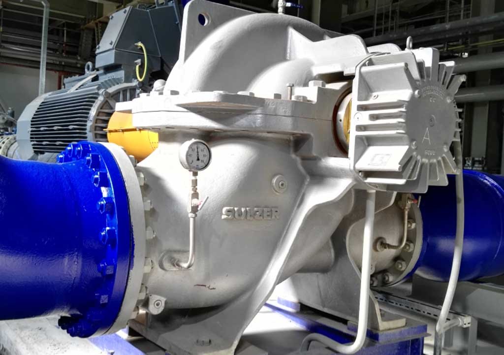 Close-up of a large industrial pump with blue pipes and a pressure gauge indoors.