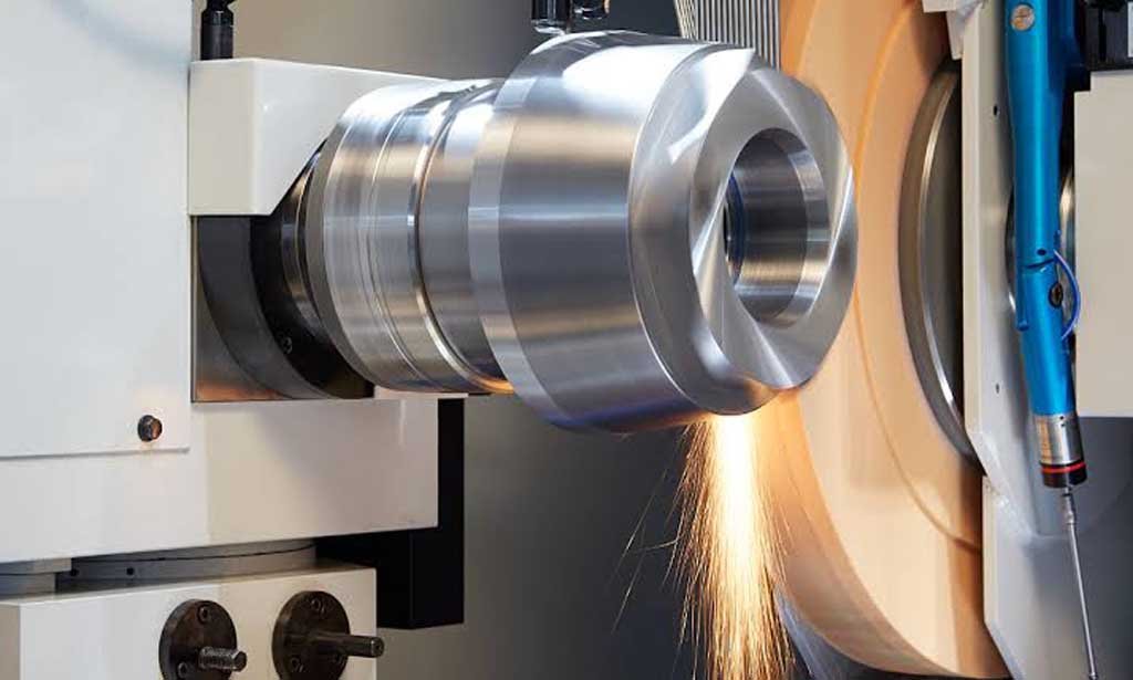 Close-up of a metal grinding machine smoothing a cylindrical metal part with sparks flying.