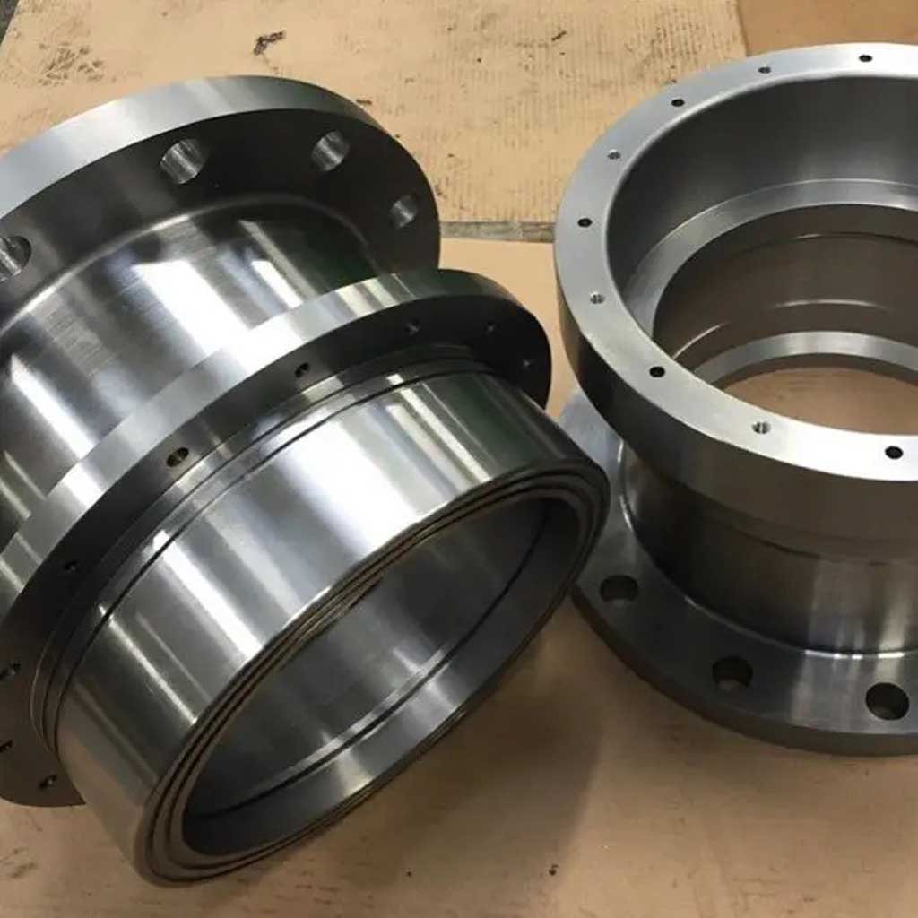 Two large cylindrical metal machine parts with flanges and bolt holes on a wooden surface.